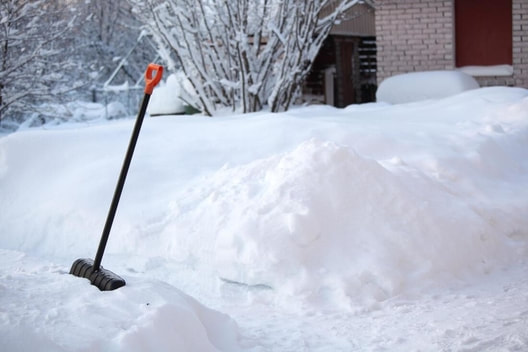 A shovel stuck in the snowbank next to freshly shoveled paths.