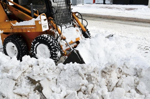 A skid steer clears the deep snow drifts, covering the driveway.